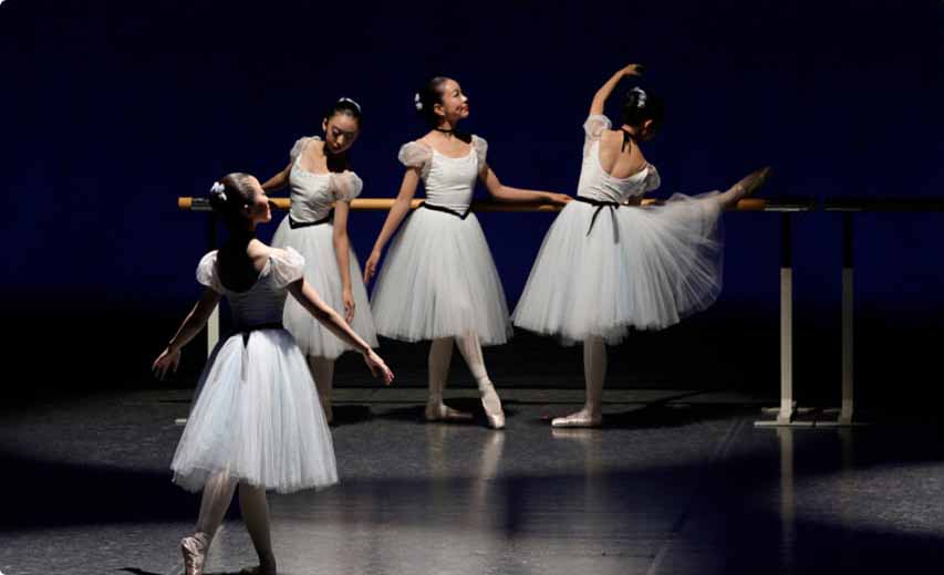 舞台中の画像 白いドレスの女の子4人 バーの前でそれぞれポーズを決める3人の女の子 前で踊る一人の女の子